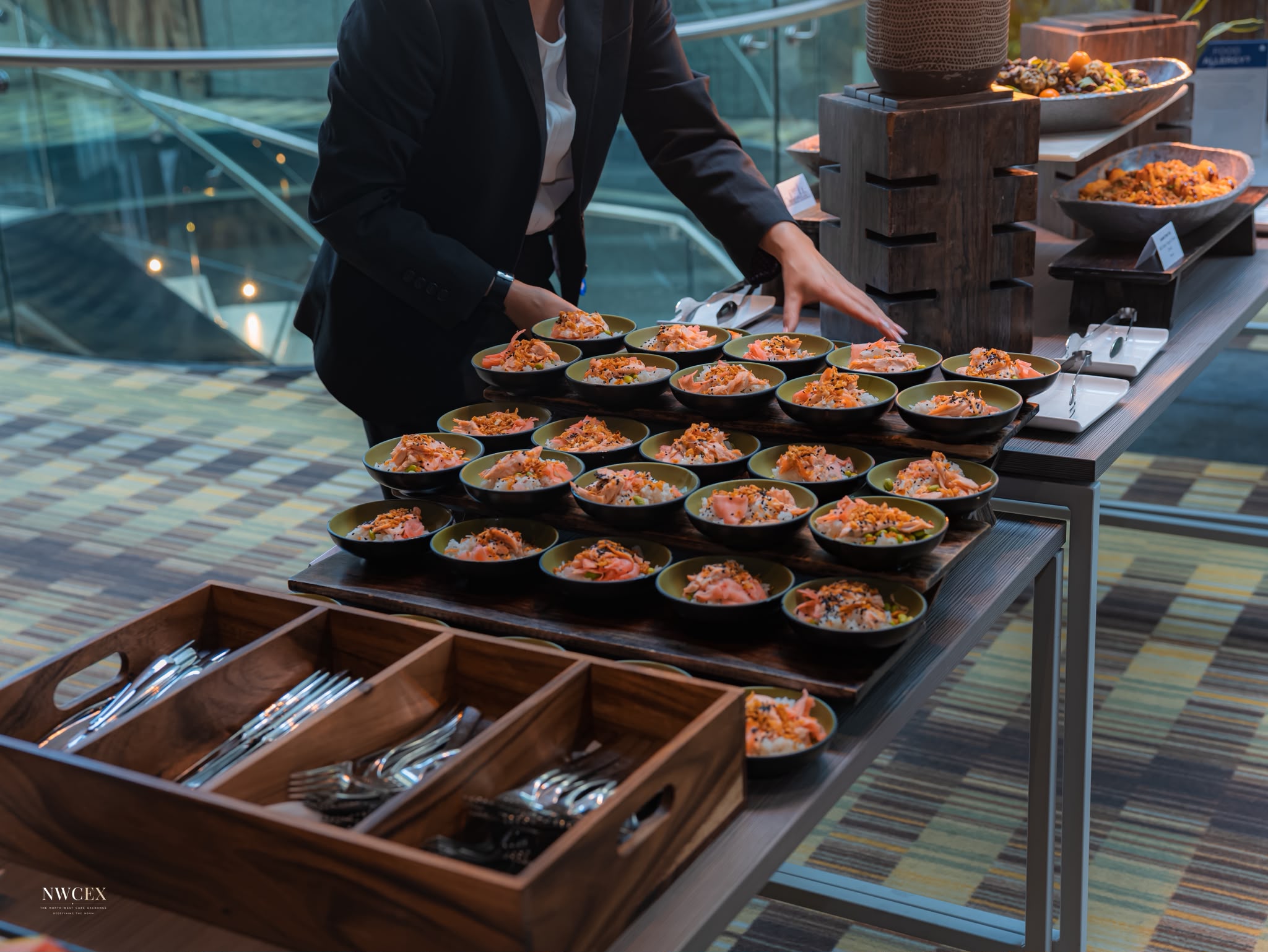 Salmon rice bowls laid out on wooden boards, with a member of the service team adjusting the display.